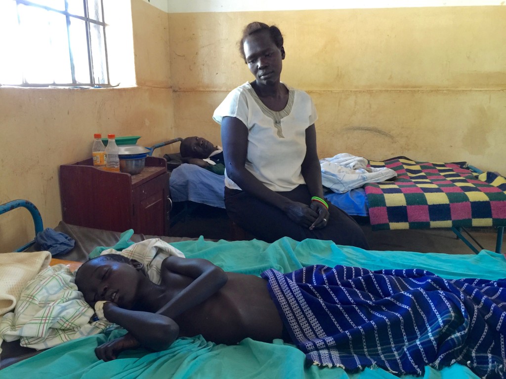 The mother sits near her son who is extremely sick with malaria.